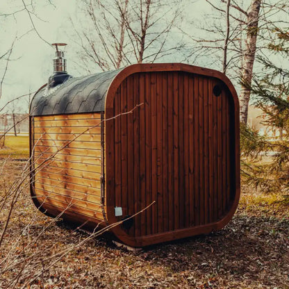 Back view of the Mande Spa USA MW20 outdoor sauna with wood-burning heater, roof shingles, metal bands, and rear exterior siding in a peaceful forest setting.