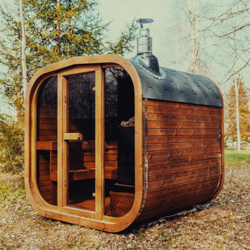 Mande Spa USA MW20 outdoor sauna with wood-burning heater, tempered glass door and windows, Bituminous roof tiles, and metal bands in a peaceful forest setting.