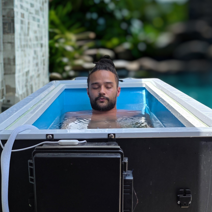 Man in  Black matte cold plunge tub at night on a dark patio with blurred outdoor background.