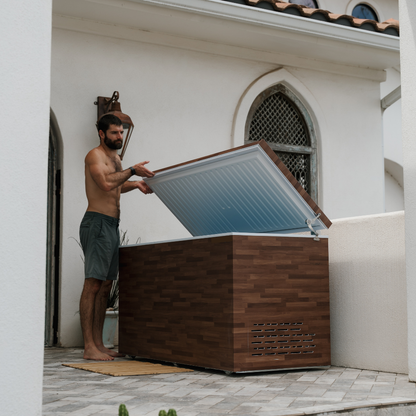 Man opening a wooden cold plunge tub with a white interior on a patio.
