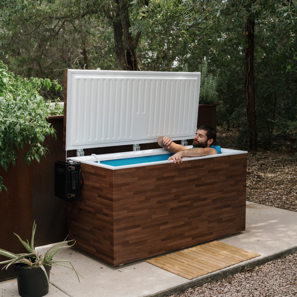 Man relaxing in cold plunge with a wooden exterior in a natural setting.
