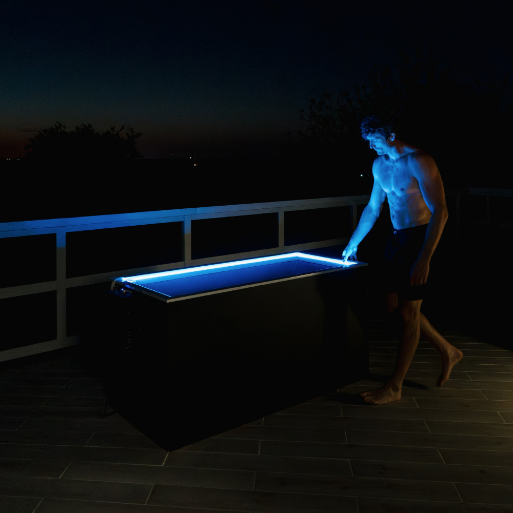 Man stays near  Black matte Plunge Zero SoftTop cold plunge tub at night on a dark patio.
