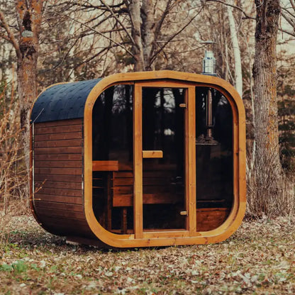Fully assembled Mande Spa USA MW20 outdoor sauna with wood-burning heater, tempered glass door and windows, Bituminous roof tiles, and metal bands in a peaceful forest setting.