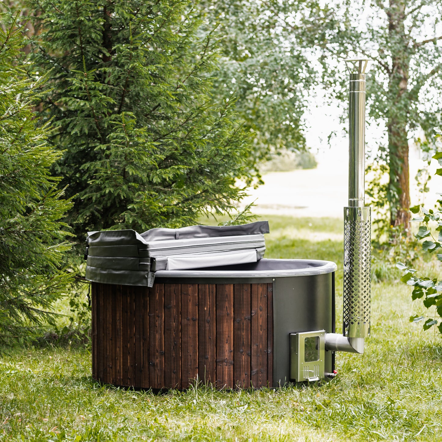 wood-fired hot tub with wooden exterior and metal chimney in a forest setting, designed for backyard relaxation and natural wellness.