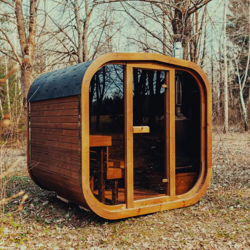 Mande Spa USA MW20 outdoor sauna with wood-burning heater, tempered glass door and windows, Bituminous roof tiles, and metal bands in a peaceful forest setting.