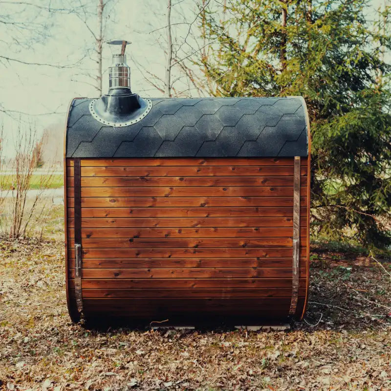 Side view of the Mande Spa USA MW20 outdoor sauna with wood-burning heater, roof shingles, metal bands, and rear exterior siding in a peaceful forest setting.